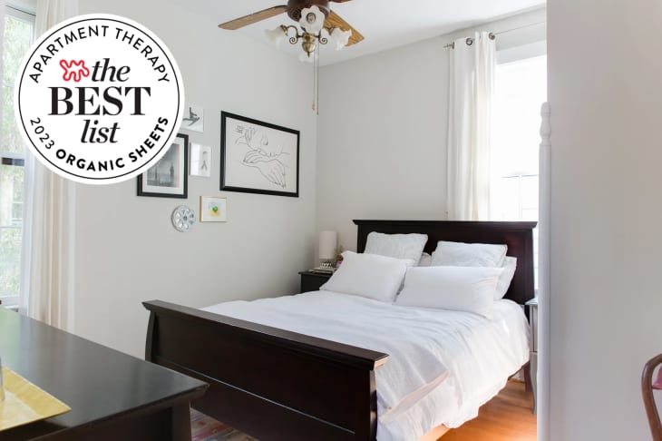 Photo of bed with white sheets, pillowcases, coverlet. White walls, wood ceiling fan, large window. There is a seal in the upper left that reads "Apartment Therapy The Best List: 2023 Organic Sheets"