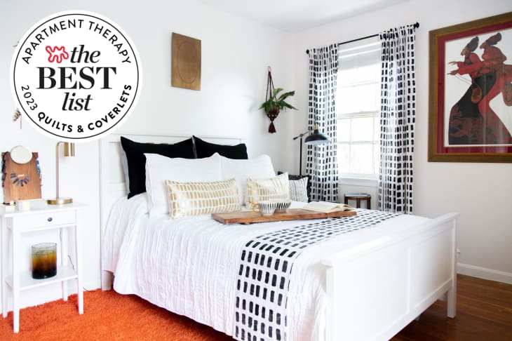 white bedroom with black and white details, orange rug. Seal in upper left reads "Apartment Therapy the Best List 2023 Quilts &amp; Coverlets"