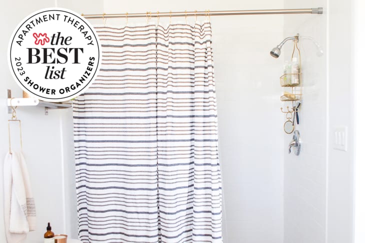 White shower with striped black and white curtain and gold shower caddy. Seal in upper left corner reads "Apartment Therapy the Best List 2023 Shower Organizers"