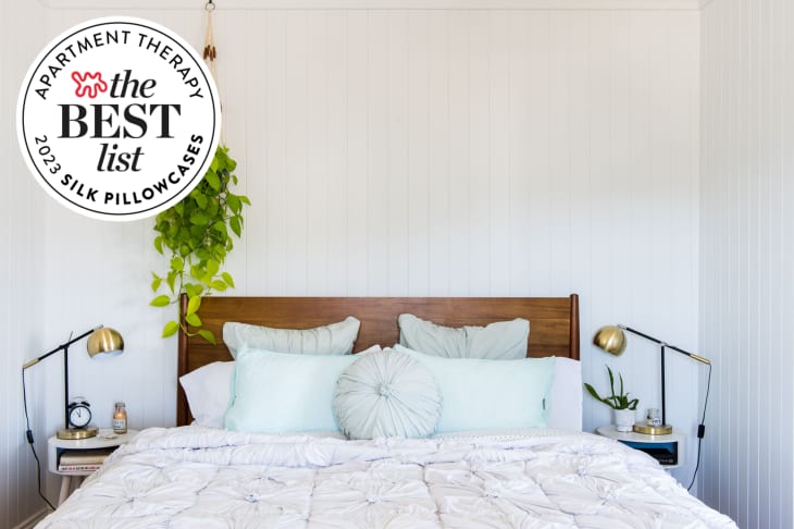 Image of bed with lots of pillows, white shiplap wall, hanging plant. Seal in upper left corner reads "Apartment Therapy The Best List 2023 Silk Pillowcases"