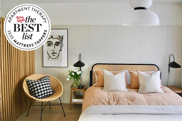 Cozy bedroom featuring a bed with peach bedding, decorative pillows, a rattan chair, and a floral arrangement.