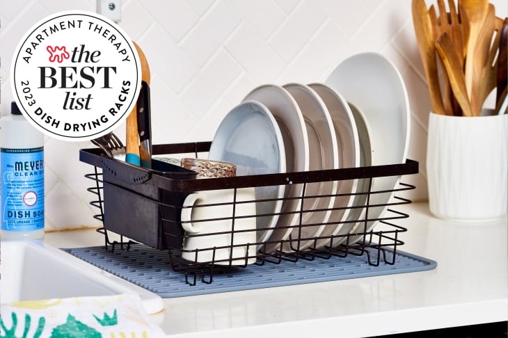 Black dish drying rack full of dishes and utensils sitting on a kitchen counter next to the sink. There is a seal in the upper left corner that reads "Apartment Therapy the Best List 2023 Dish Drying Racks"