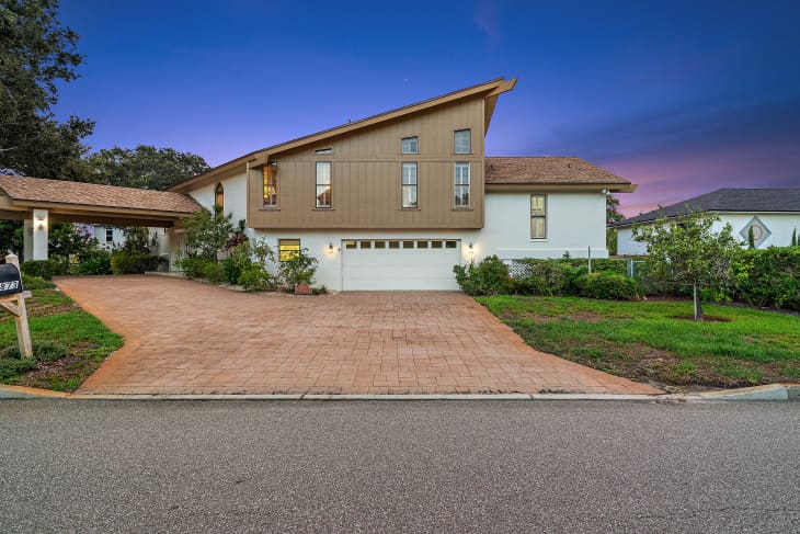 Modern two-story house with sloped roof, large driveway, and landscaped front yard at dusk.