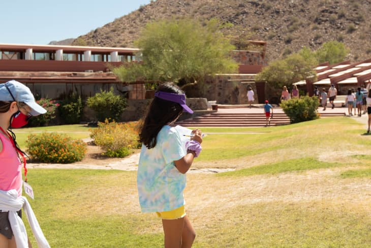 Two girls walking on a grassy area near a building with desert hills in the background.