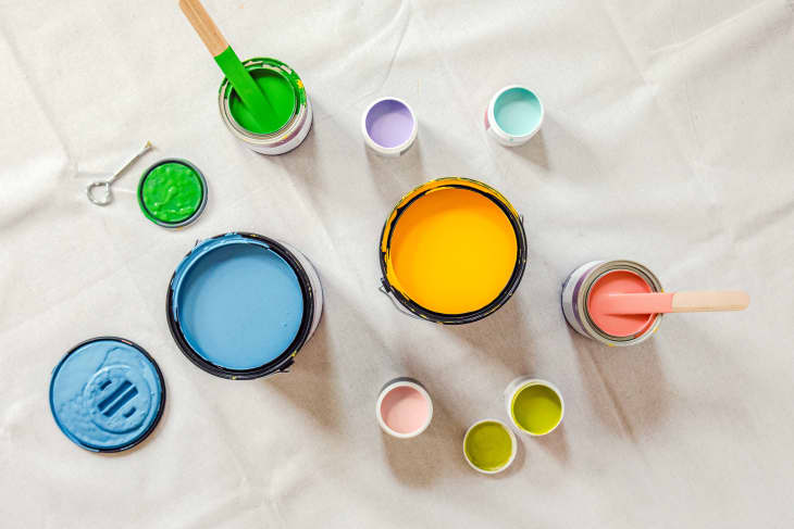 various bright colored paints in different sizes shot overhead. a can opener and a stirring stick in photo