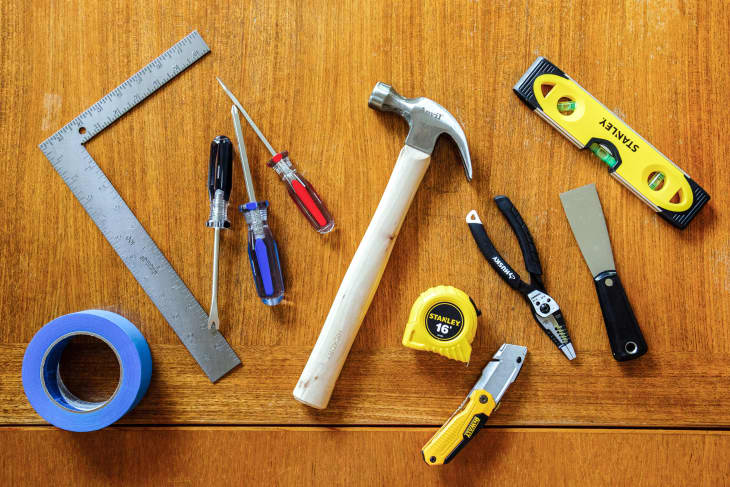 collection of tools (hammer, ruler, level, pliers, measuring tape, screwdrivers) on a wood surface