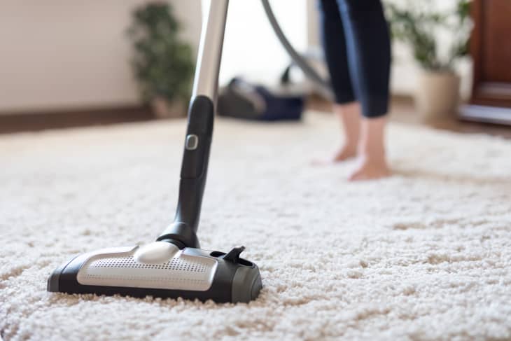 A person holds a vacuum cleaner and places it onto the carpet