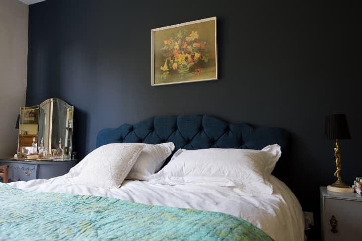 A bed with a navy headboard in front of a black wall.