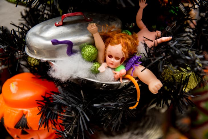Creepy doll with red hair in a metal pot, surrounded by Halloween decorations and black tinsel.