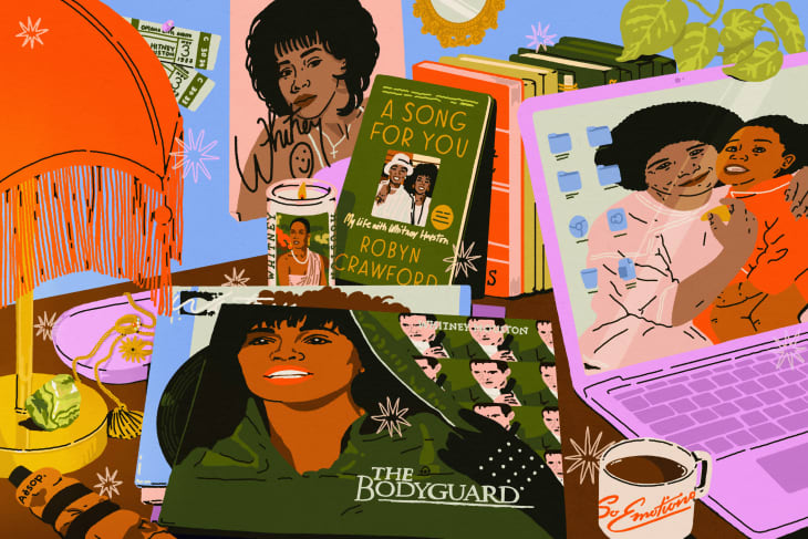 Desk with Whitney Houston memorabilia, including a book, vinyl, candle, and laptop with a family photo on the screen.