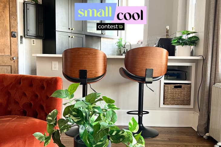 Kitchen counter with two wooden bar stools, a red velvet chair, and green plants.