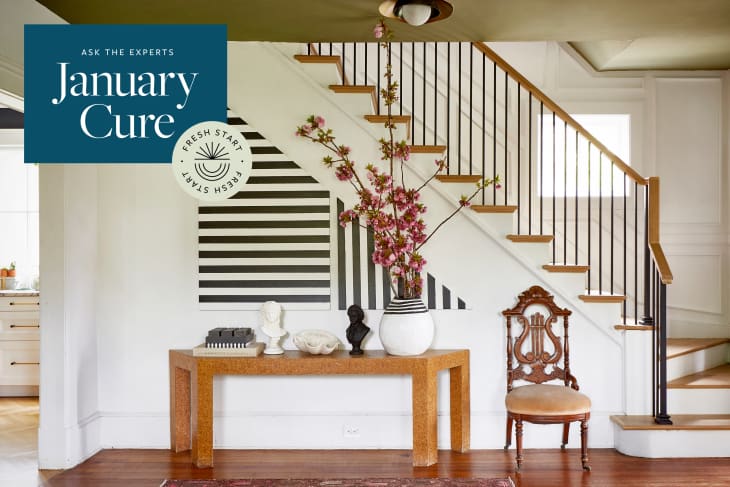 Staircase with black railings, wooden steps, a console table with a vase of pink flowers, and an ornate wooden chair.