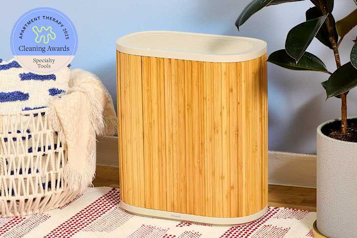 Bamboo air purifier next to a woven basket with a blue and white blanket, and a potted plant on a patterned rug.