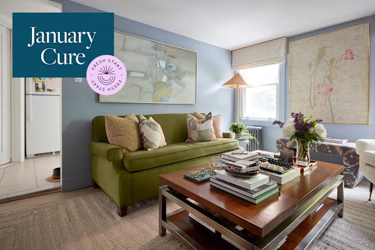 Cozy living room featuring a green sofa with patterned pillows, a wooden coffee table stacked with books, and floral decor.