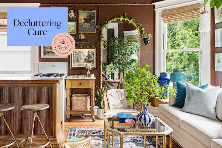Cozy living space with a beige sofa, blue and white decor, plants, and a wooden kitchen bar.