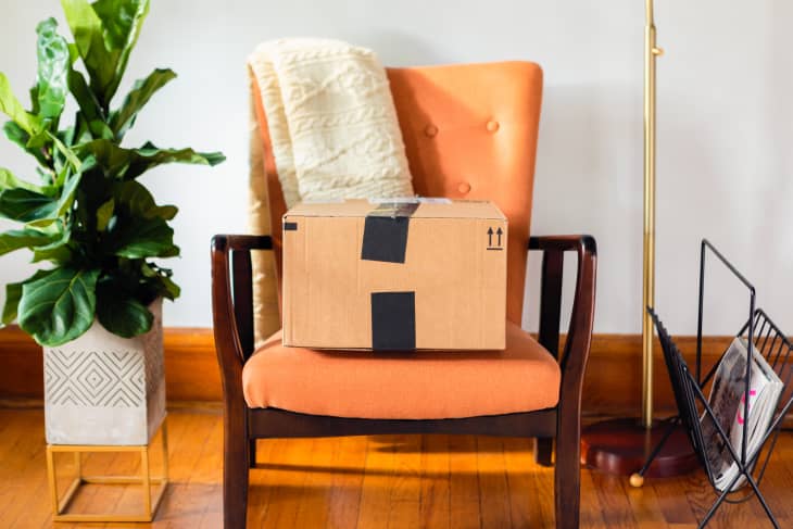 A taped-up cardboard box sitting on an orange chair inside a home, waiting to be mailed