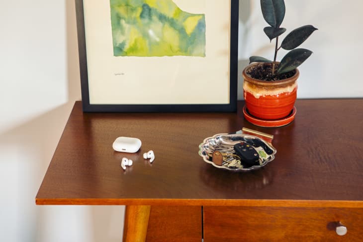 Apple airpods headphones on a wooden entryway table next to keys and a houseplant