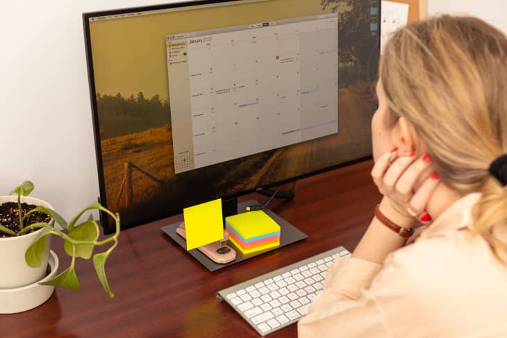 A woman sitting at a computer desk, reviewing a digital calendar app