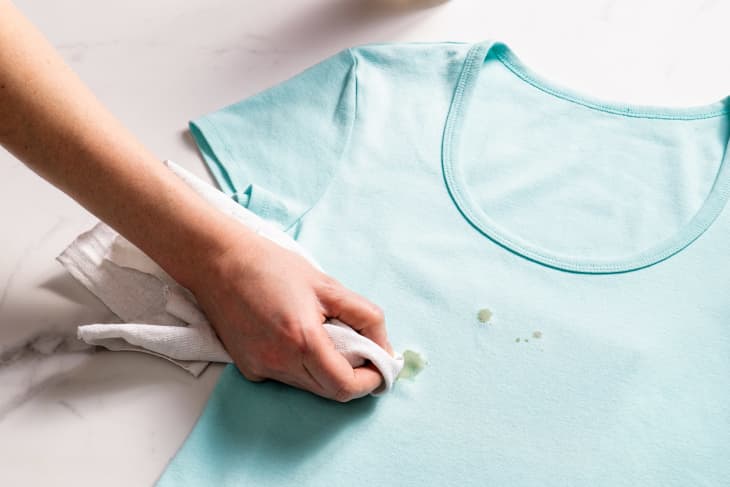 person blotting an oil stain on a aqua t-shirt on white marble surface