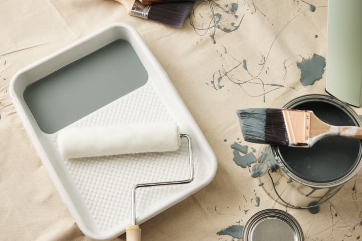 paint scattered on a canvas with paint can, paint roller and tray, and brushes around