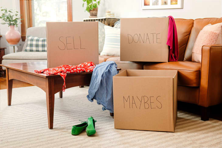 Living room with 3 "outboxes" for decluttering, one labeled "Sell", one labeled "Donate", and one labeled "Maybe". There are clothes and shoes around