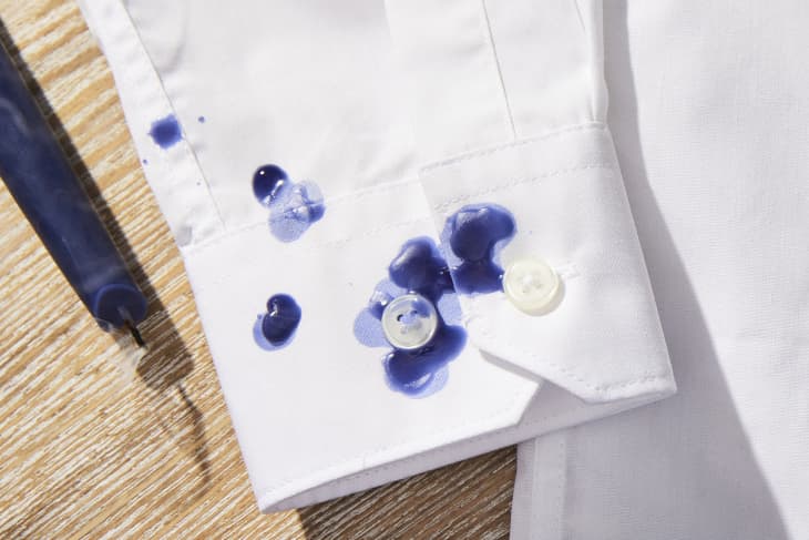 Cuff of white shirt stained with blue candle wax. Candle sitting on table nearby