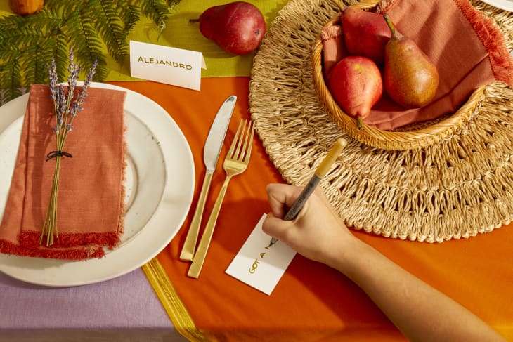 Overhead view of a hand writing out a place card on a colorful holiday table.