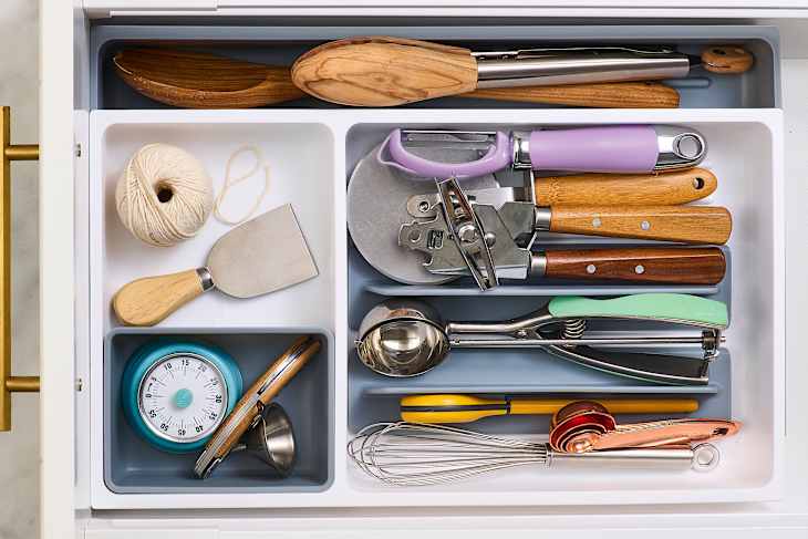 Kitchen drawer filled with various utensils including wooden spoons, a timer, measuring cups, and a whisk.