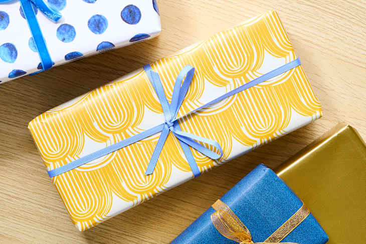 Three beautifully wrapped gifts on a wooden surface: one with blue polka dots, one with yellow patterned paper, and one in blue with an orange ribbon.