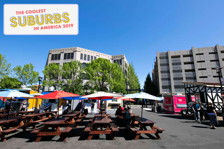 Outdoor food court with colorful umbrellas, picnic tables, and food trucks under a clear blue sky.