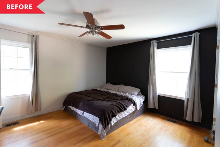 Bedroom with a dark accent wall, bed with brown bedding, wooden floor, ceiling fan, and two windows with curtains.