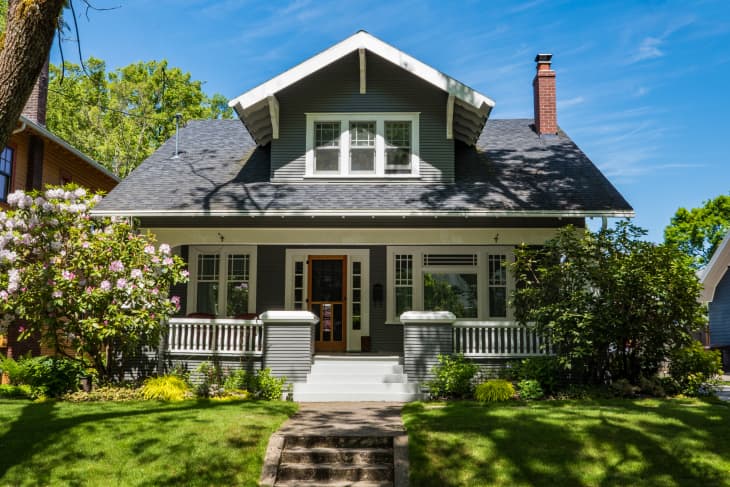 Gray craftsman-style house with a gabled roof, front porch, and lush garden.