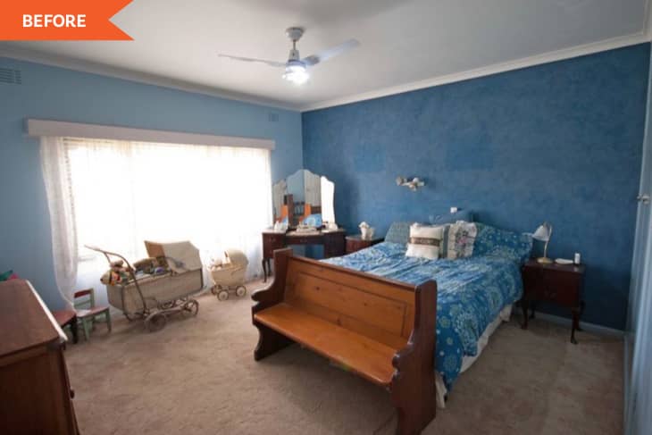 Blue bedroom with a wooden bench, vintage pram, and vanity table, featuring a blue floral bedspread and ceiling fan.