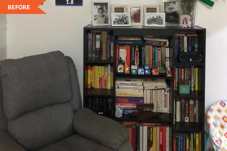 Gray recliner next to a dark wood bookshelf filled with books, toy trucks, framed photos, and a small speaker.