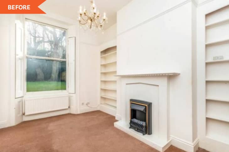 Empty room with brown carpet, white walls, built-in shelves, a fireplace, large window, and chandelier.