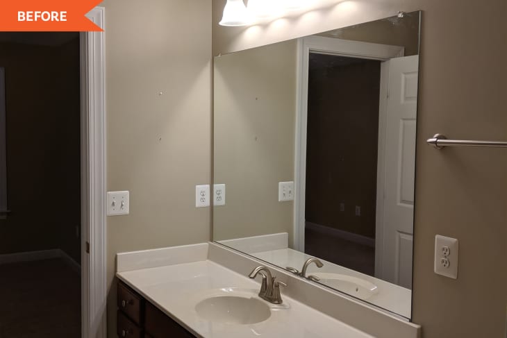 Bathroom with large mirror, beige walls, white countertop, and silver faucet under bright lighting.