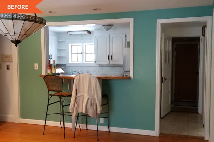 Kitchen pass-through with wooden counter, two wicker bar stools, teal walls, and a hanging stained glass light fixture.