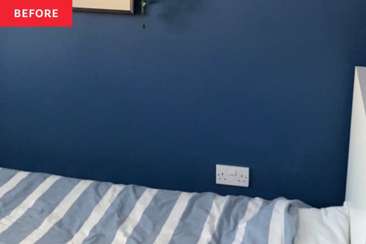 Blue bedroom wall with a striped gray and white bedspread and a wall socket.