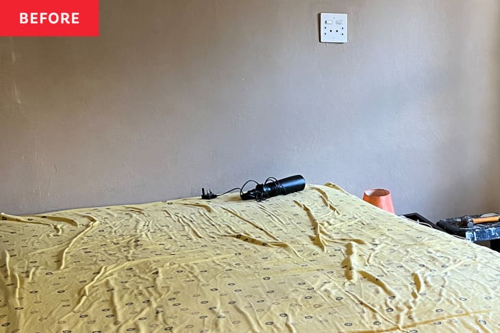 Unmade bed with yellow sheet, black water bottle, and orange lamp on bedside table.