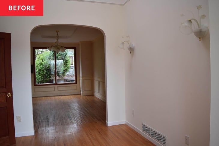 Empty dining room with wooden floor, large window, chandelier, and wall sconces.