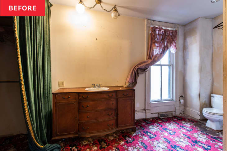 Bathroom with floral carpet, wooden vanity, green curtain, and window with pink drapes.