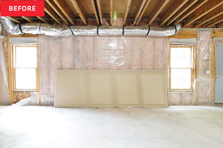 Basement wall with drywall panel laying on floor before renovation.