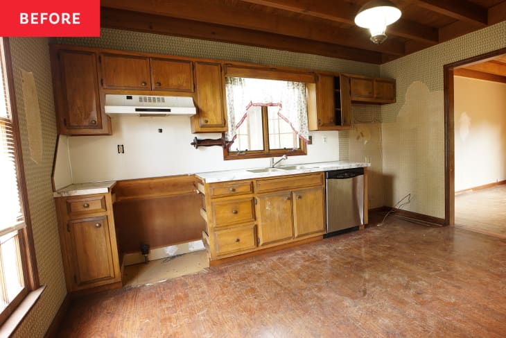 Kitchen before renovation. Ambered wood cabinets, rust-colored floor, no stove in place