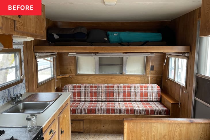 Camper with dark wooden interior and plaid sofa before renovation.