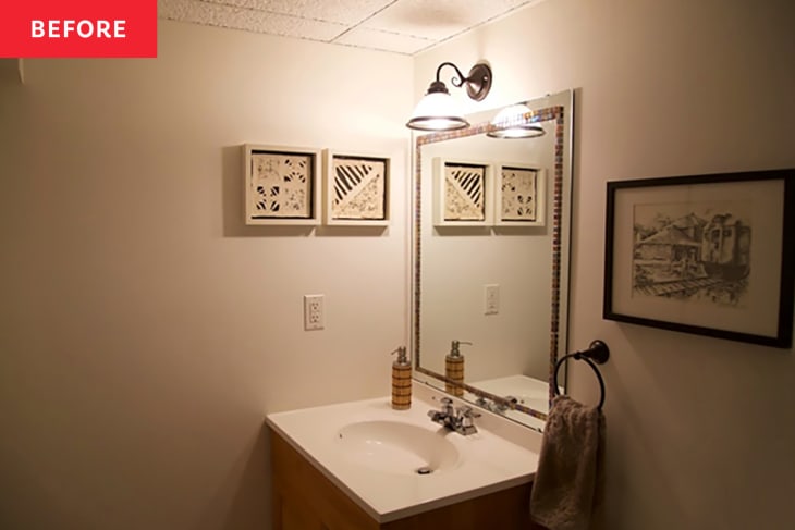 Sconce over mirror in bathroom with art on walls before renovation.