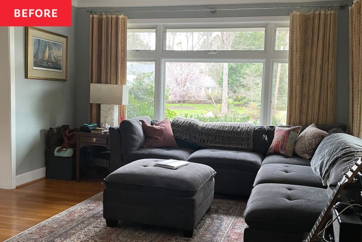 living/family room before makeover. Dark gray sectional, beige curtains, large window, gray walls with white trim