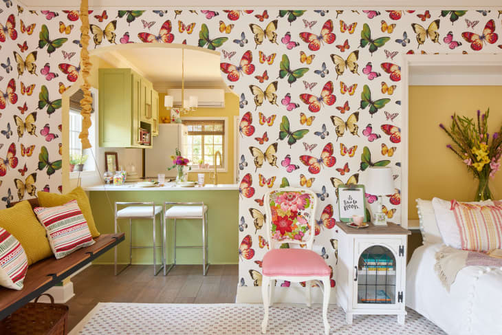 green, yellow, and red butterfly wallpaper, arched cut out to kitchen, bench floating on wall, pink vintage upholstered chair
