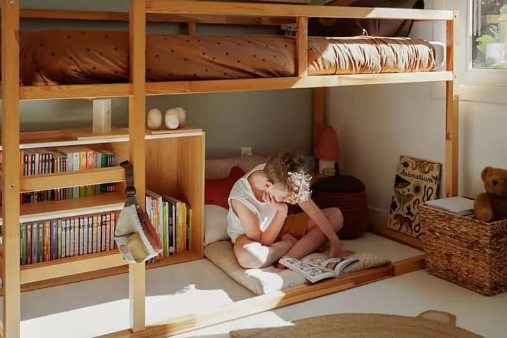 Child sitting on the floor reading under a bunk bed.