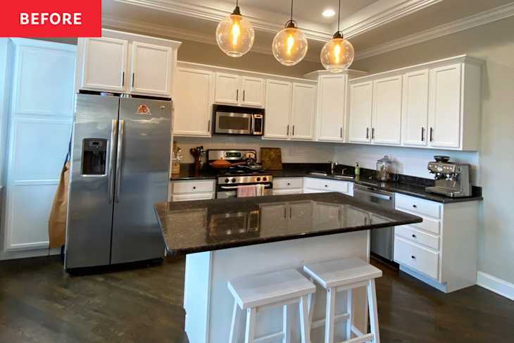 Modern kitchen with white cabinets, stainless steel appliances, black countertops, and three pendant lights above an island with stools.