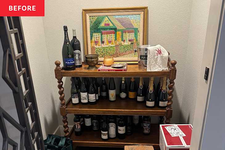Wooden shelf displaying various wine bottles, a decorative painting, and a metal bucket, with a green bag nearby.